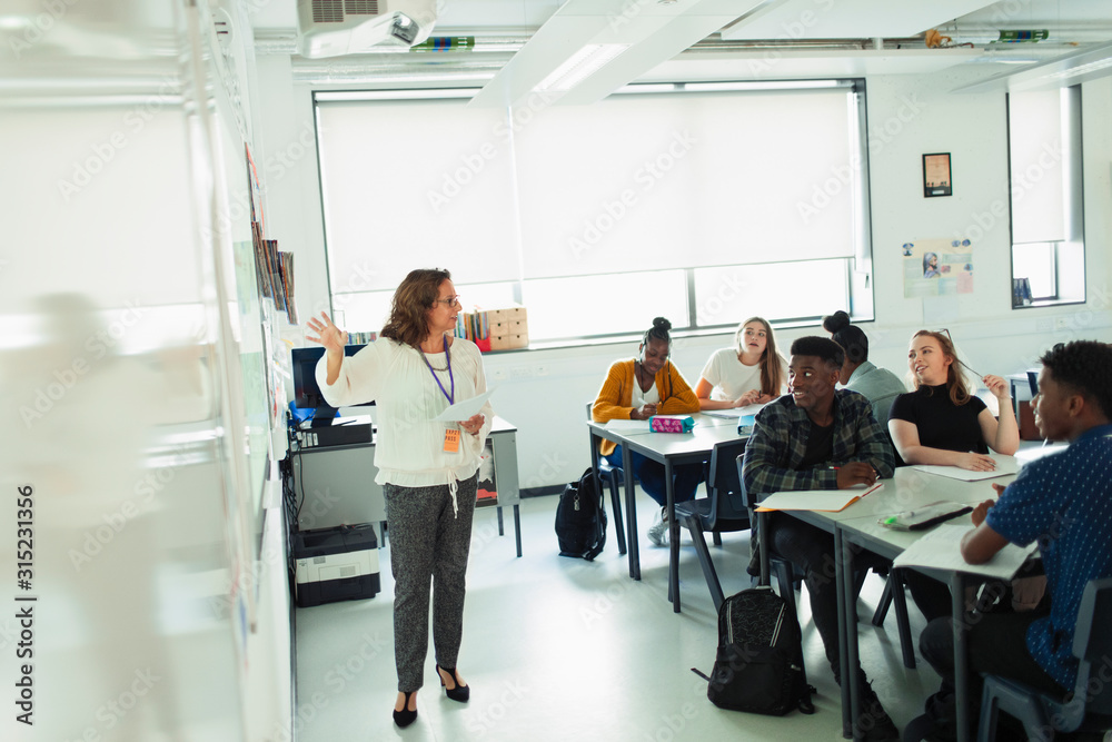 High school students watching teacher leading lesson at whiteboard in classroom High school students watching teacher leading lesson at whiteboard in classroom