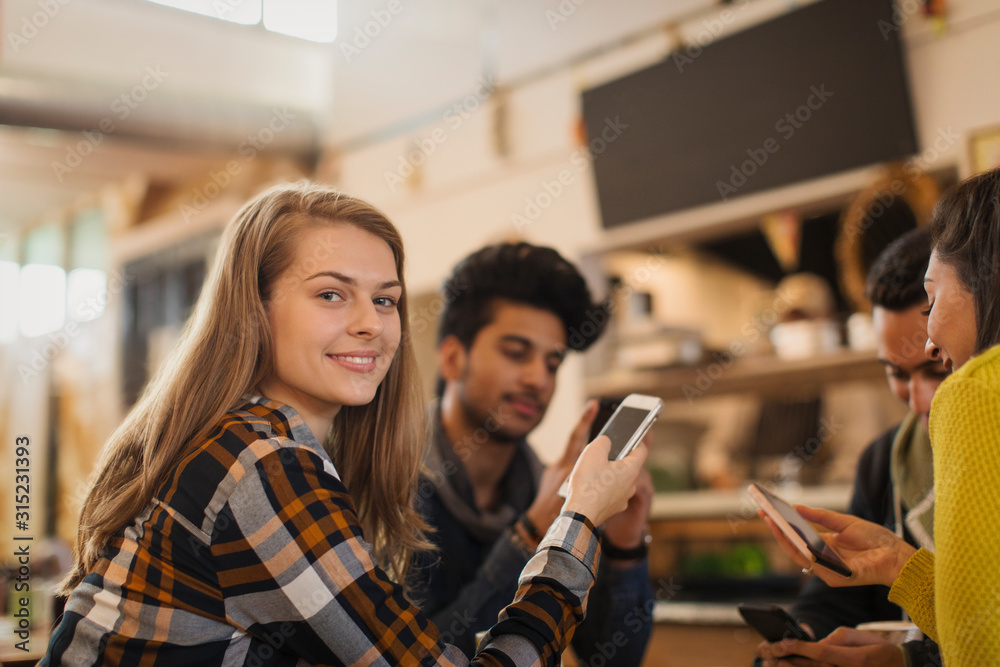 Portrait confident young woman using smart phone in cafe with friends Portrait confident young woman using smart phone in cafe with friends