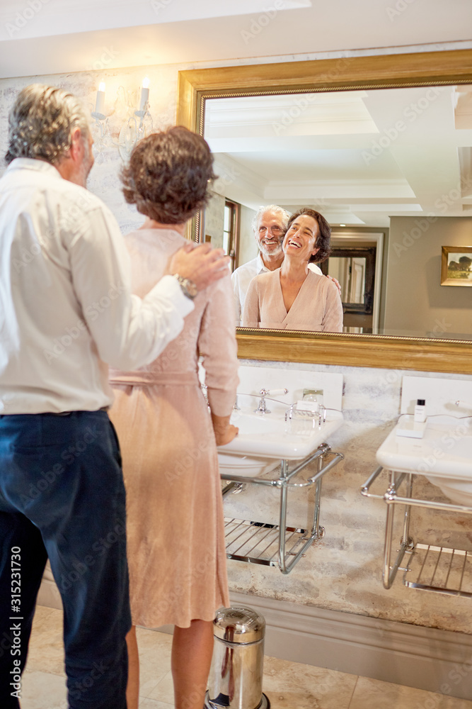 Happy mature couple standing at hotel bathroom mirror Happy mature couple standing at hotel bathroom mirror