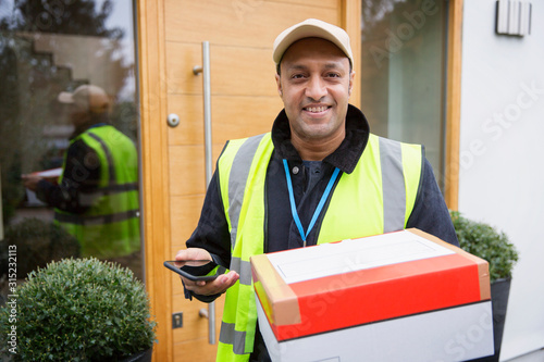 Portrait confident, friendly deliveryman with package and smart phone at front door