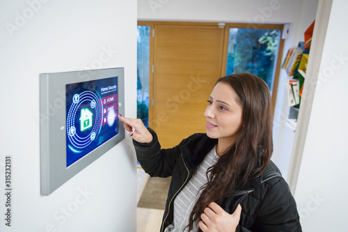 Woman leaving house, setting smart home alarm photo