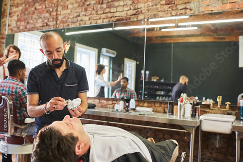 Male barber preparing to shave face of customer in barbershop photo