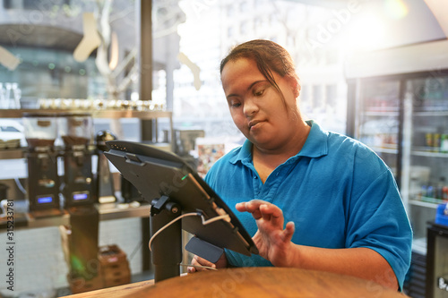 Young woman with Down Syndrome working at cash register in cafe photo