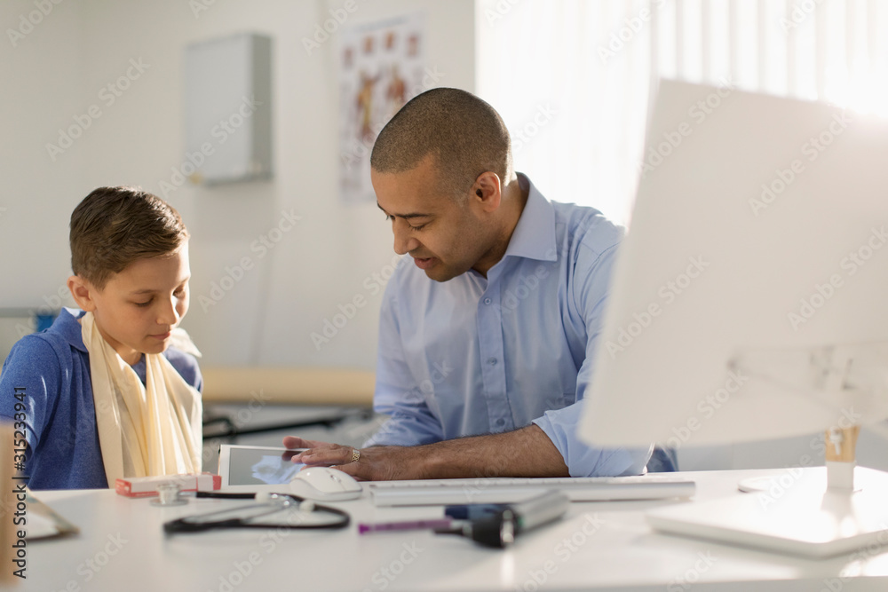 Male pediatrician showing digital x-ray to boy with arm in sling in doctors office Male pediatrician showing digital x-ray to boy with arm in sling in doctors office