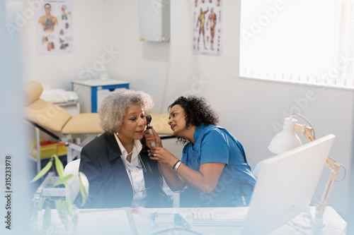 Female doctor examining ear of senior patient with otoscope in doctors office photo