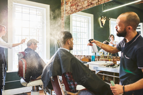 Male barber spraying hair of customer in barbershop photo