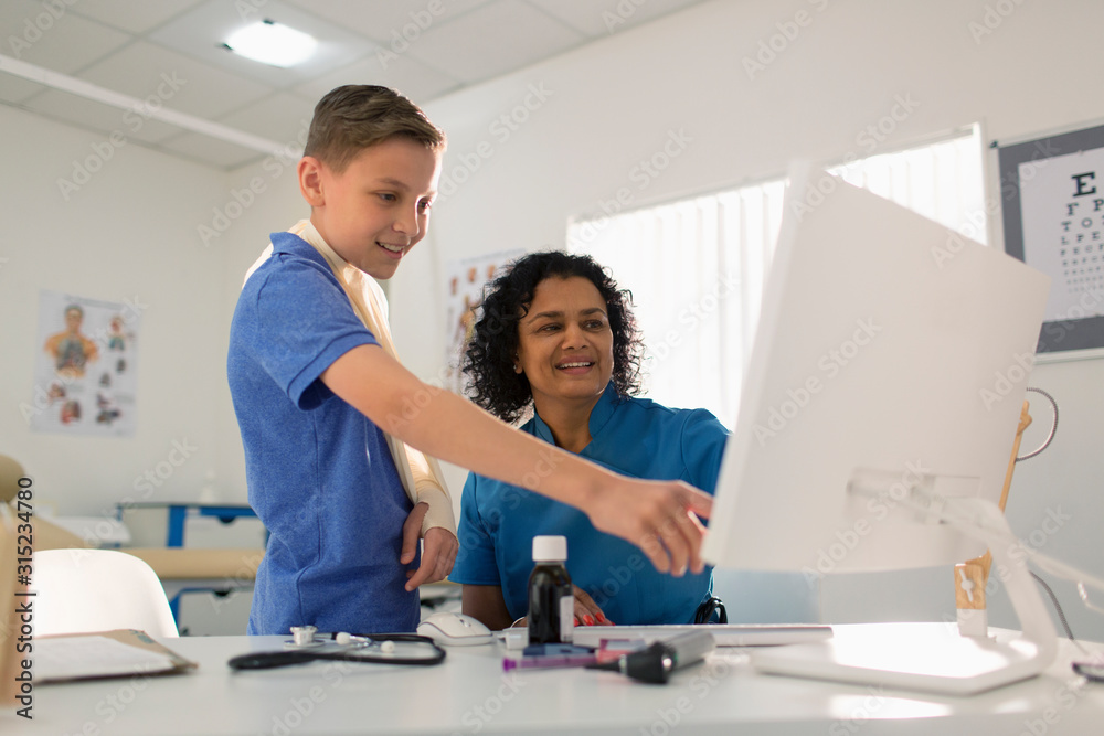 Female pediatrician and boy patient using computer in doctors office Female pediatrician and boy patient using computer in doctors office