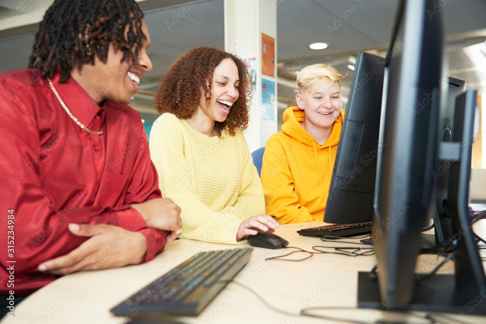 Happy college students studying together at computer in library Happy college students studying together at computer in library