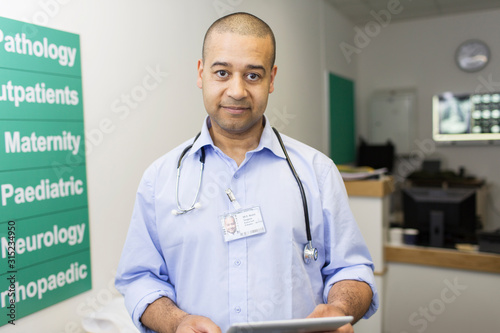 Portrait confident male doctor with digital tablet in hospital corridor photo