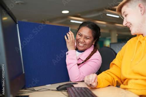 Happy young female college students laughing at computer in library photo