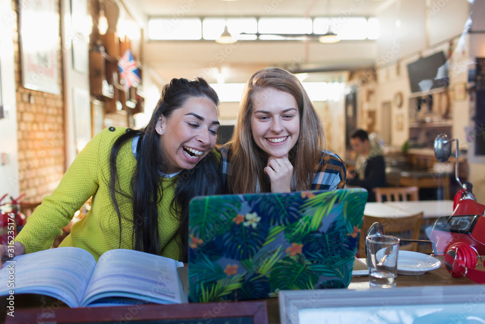 Happy, laughing young female college students using laptop in cafe window Happy, laughing young female college students using laptop in cafe window