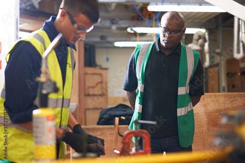 Shop class teacher watching student in workshop photo