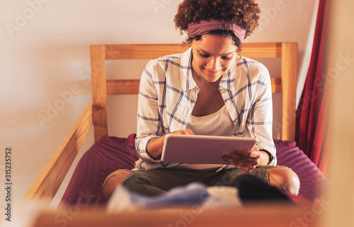 Young female college student using digital tablet on dorm room bunk bed