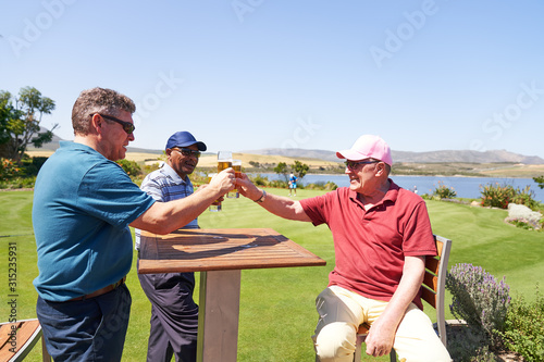 Mature male golfers drinking beer on sunny golf clubhouse patio photo