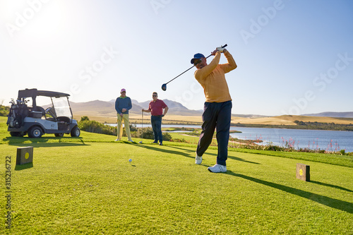 Male golfer teeing off at sunny golf tee box photo