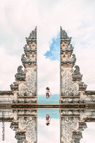 A girl is jumping in front of the Gate of Heaven with its reflection in the water. Bali, Indonesia.