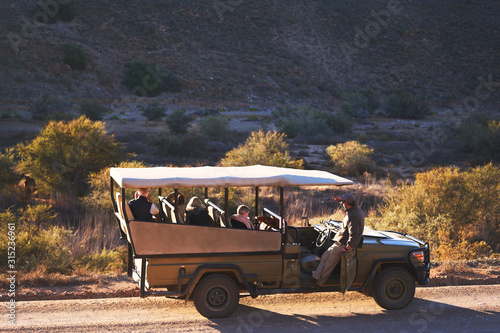 Safari tour guide and group in off-road vehicle on sunny dirt road photo