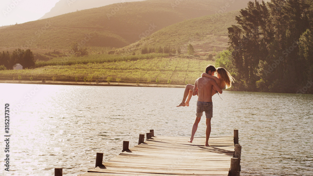 Young man carrying woman on sunny lakeside dock