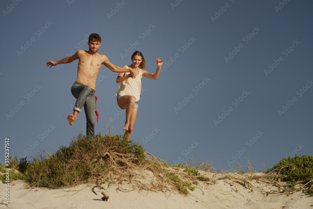 Playful young couple jumping on sandy beach Playful young couple jumping on sandy beach