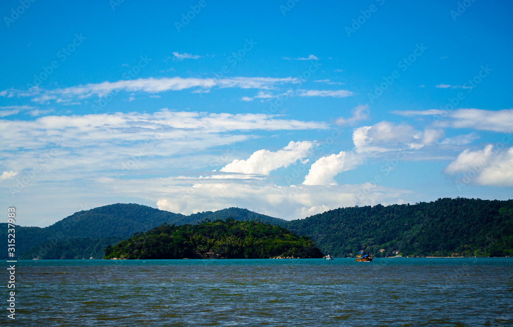 Dark sea with green island and mountains in the background with blue and cloudy sky
