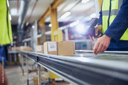 Worker scanning and processing boxes on conveyor belt in distribution warehouse