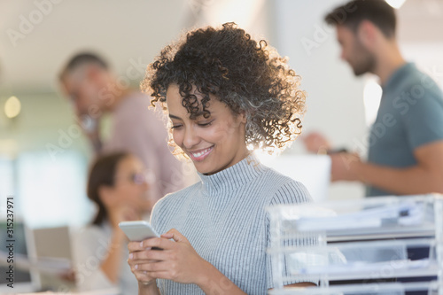 Smiling businesswoman texting with cell phone in office