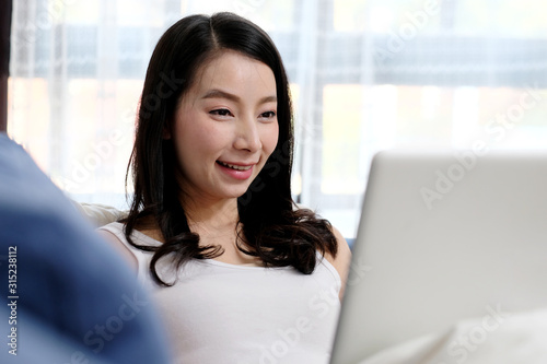 Happy asian woman using laptop computer with smiling while lying on sofa in living room, Asia female and laptop at home, people and technology, lifestyle, e commerce, online education, internet of th