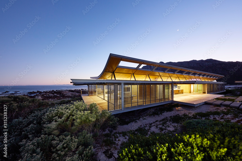Illuminated modern luxury home showcase exterior with ocean view at dusk Illuminated modern luxury home showcase exterior with ocean view at dusk