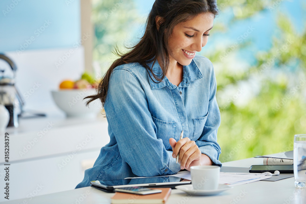 Smiling woman working reviewing paperwork at kitchen counter Smiling woman working reviewing paperwork at kitchen counter