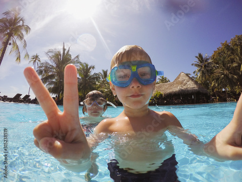 Portrait of boy gesturing peace sign in tropical swimming pool