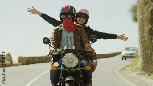 Exuberant young woman riding motorcycle on sunny road