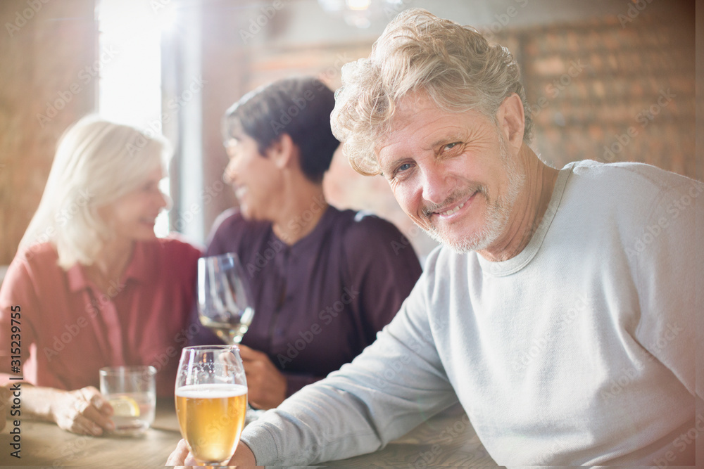 Portrait smiling senior man drinking beer dining with friends at restaurant table Portrait smiling senior man drinking beer dining with friends at restaurant table