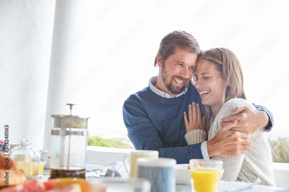 Smiling affectionate couple hugging at patio breakfast table Smiling affectionate couple hugging at patio breakfast table