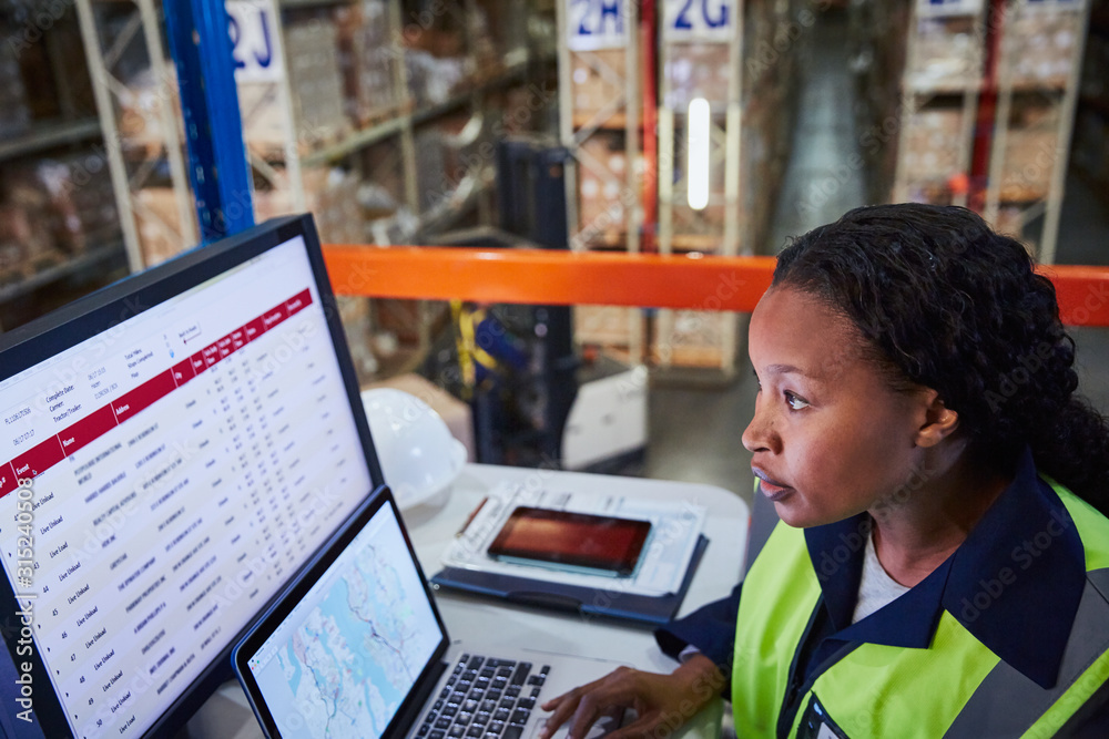 © Ryan Lees/Caia Image - Focused female manager using laptop and computer in distribution warehouse