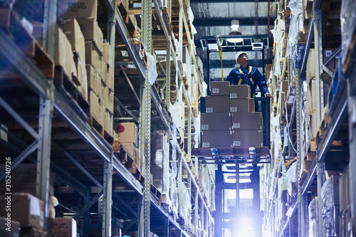 Worker operating forklift stacking cardboard boxes on distribution warehouse shelves photo