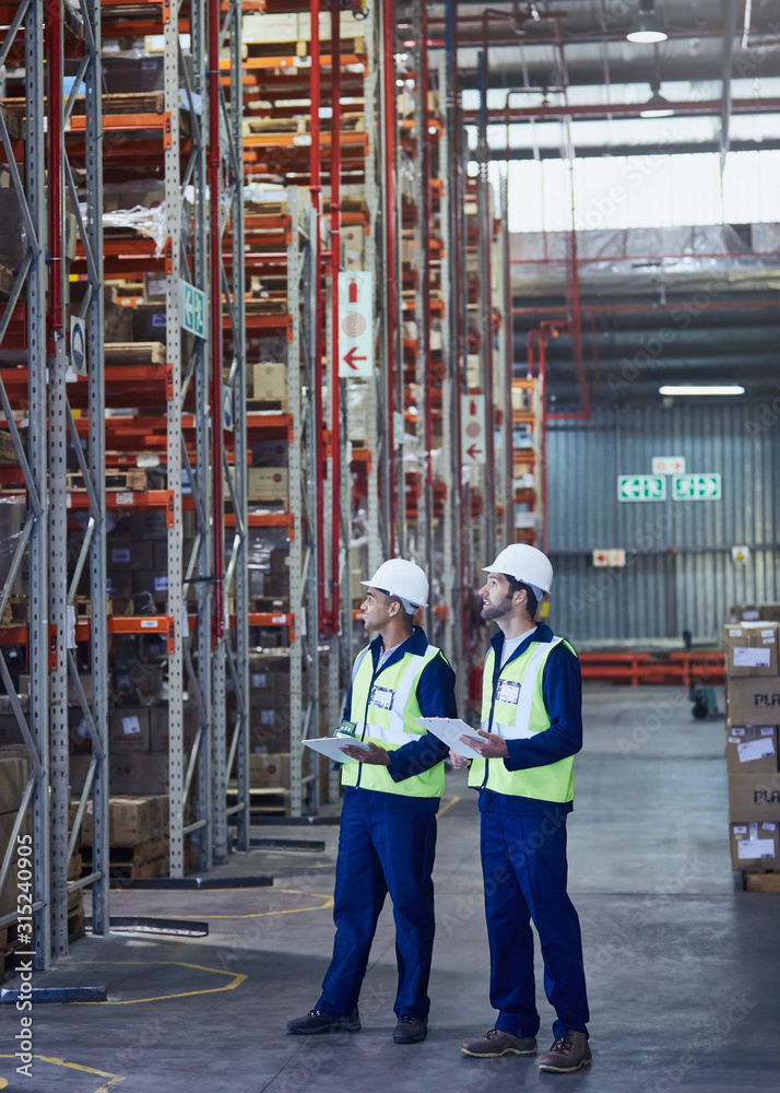 Workers with clipboards looking away in distribution warehouse Workers with clipboards looking away in distribution warehouse