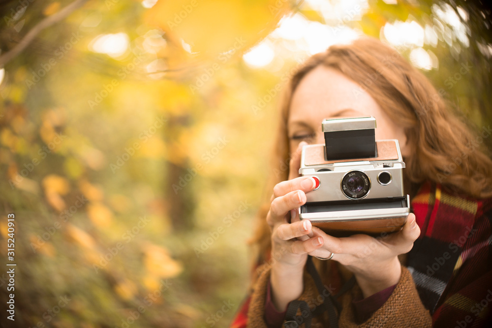 Portrait woman using old-fashioned instant camera in autumn woods Portrait woman using old-fashioned instant camera in autumn woods