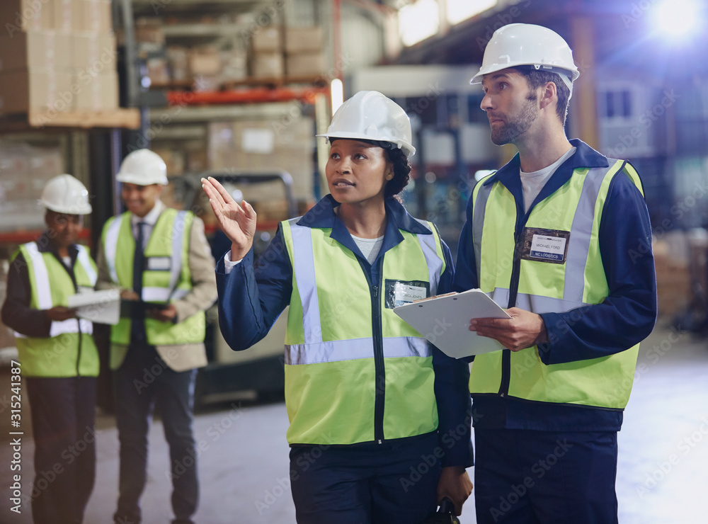 Workers with clipboard talking in distribution warehouse Workers with clipboard talking in distribution warehouse