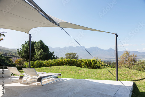 Lounge chairs under awning on sunny patio with mountain view photo