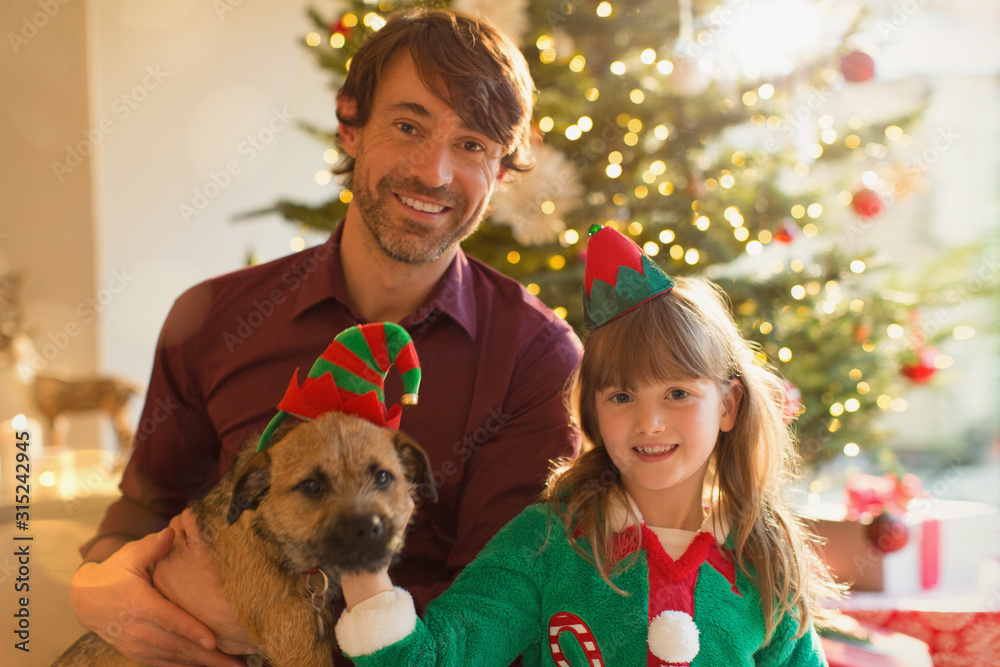 Portrait smiling father, daughter and dog in front of Christmas tree Portrait smiling father, daughter and dog in front of Christmas tree