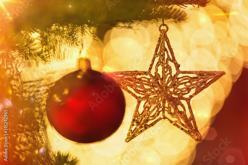 Close up red ornament and gold star hanging from branch of Christmas tree photo