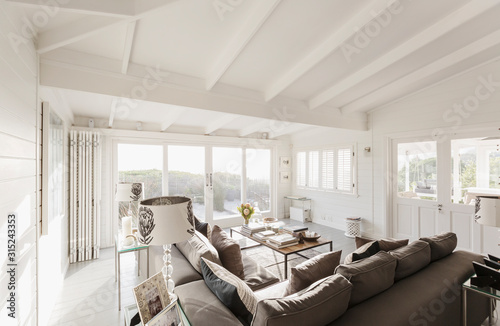 Sunny luxury home showcase living room with white wood beam vaulted ceiling