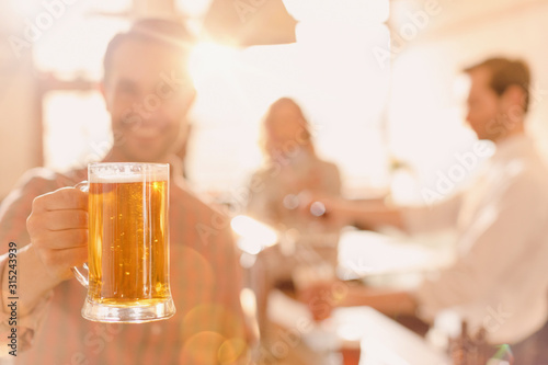 Portrait smiling man holding beer stein at brightly lit bar