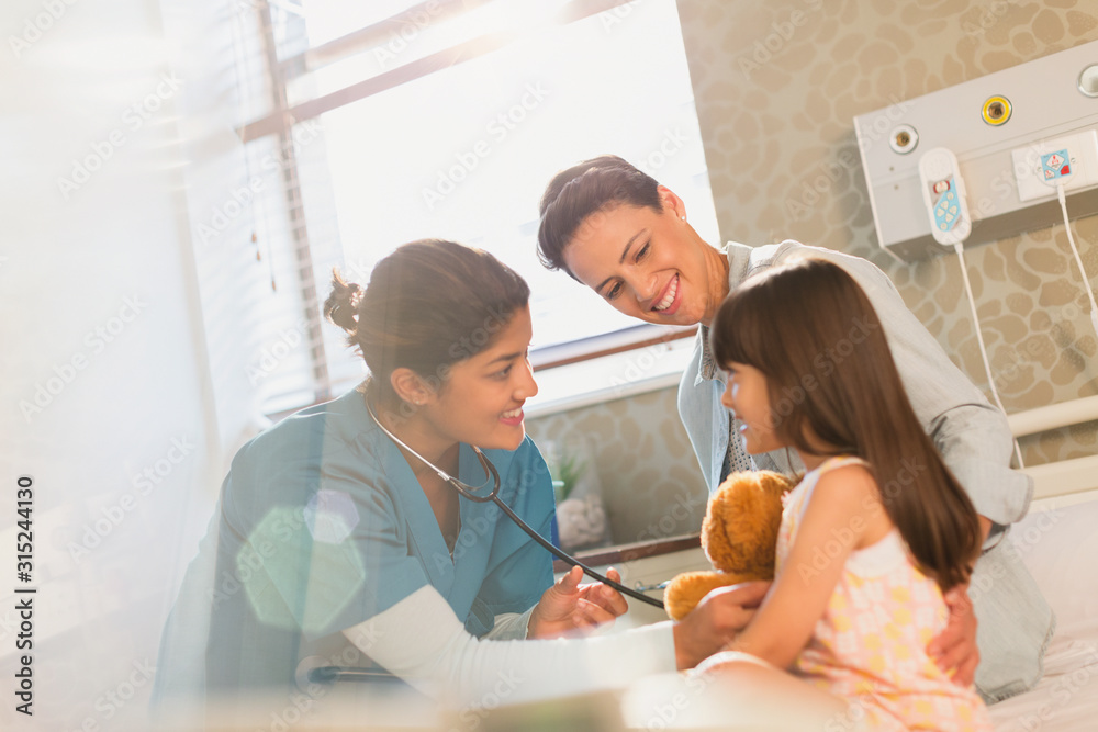 Smiling female nurse using stethoscope on girl patient in hospital room Smiling female nurse using stethoscope on girl patient in hospital room