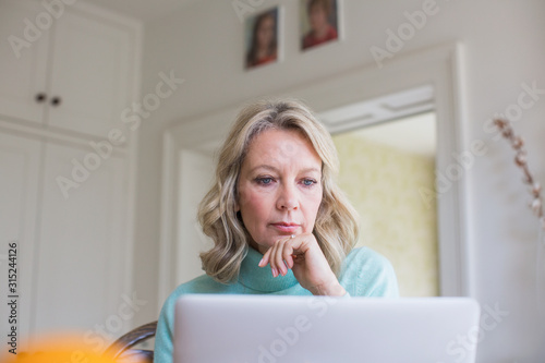 Focused mature female freelancer working at laptop at home