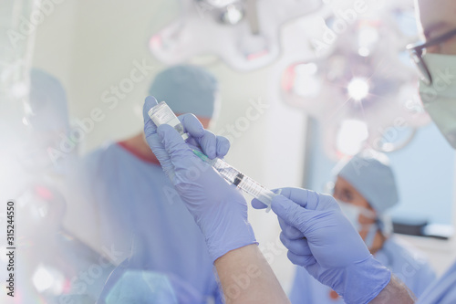Male anesthesiologist with syringe preparing anesthesia medicine in operating room photo
