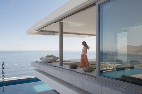 Woman looking at ocean view on modern, luxury home showcase exterior balcony photo