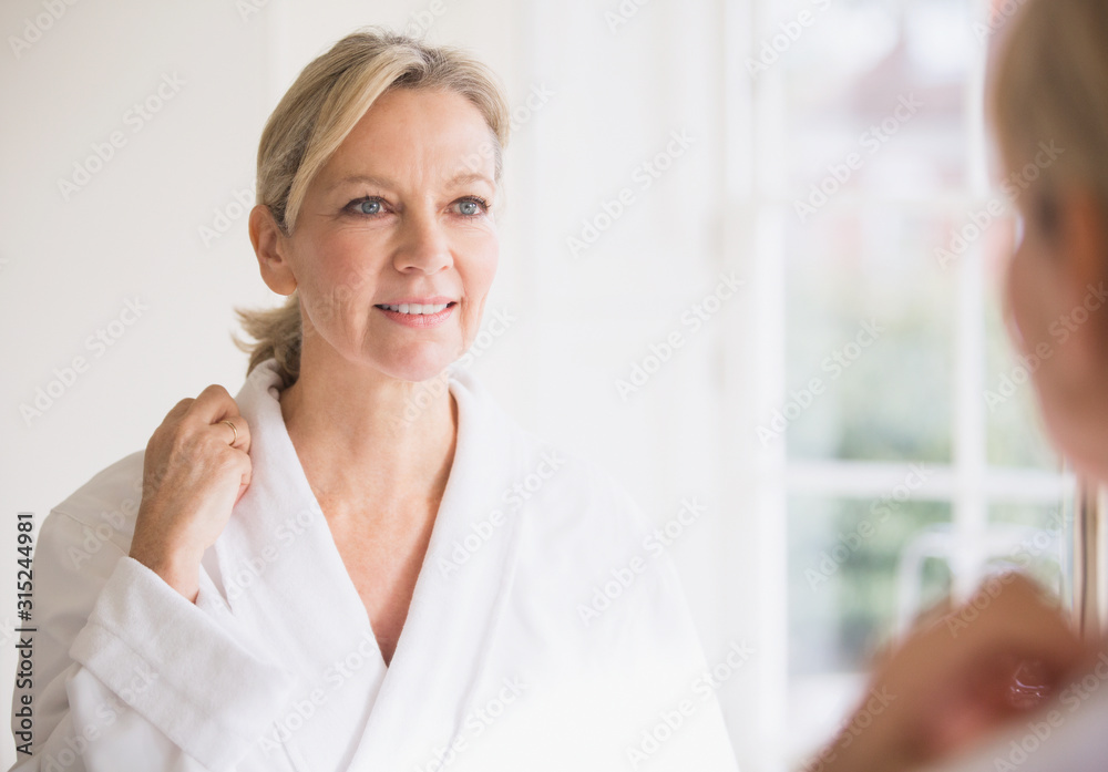 Smiling mature woman in bathrobe at bathroom mirror Smiling mature woman in bathrobe at bathroom mirror