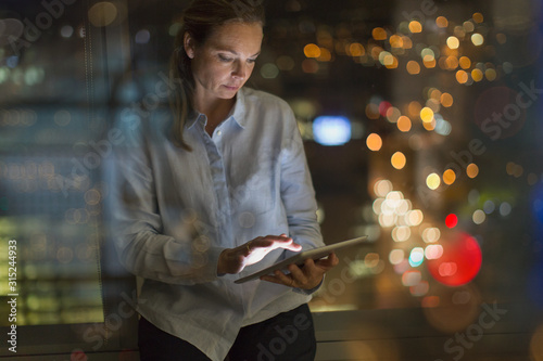 Businesswoman working late at digital tablet in office at night photo