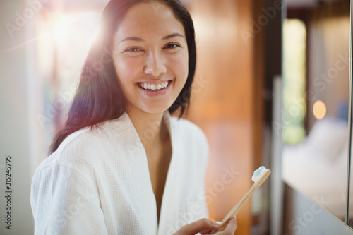 Portrait happy young woman brushing teeth in bathroom photo